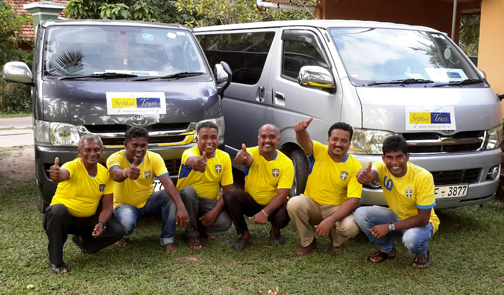 En bild på srilankanska chaufförer med svenska landslagströjor. De poserar framför minibussar med logotypen för Sophie Tours.