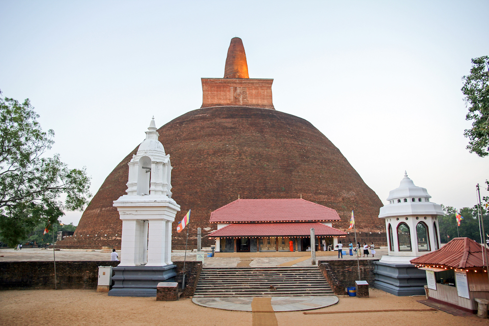 En bild på ett stort kupolformat stentempel i Anuradhapura. En trappa framför och träd med himmel i bakgrunden.