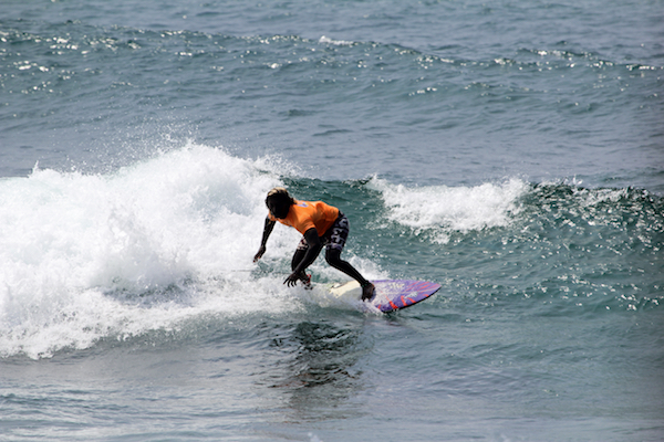 En bild på en surfare som surar på en liten våg med havet som bakgrund.